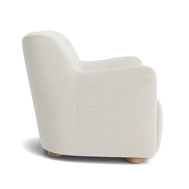 Beige upholstered chair with cylindrical bolster pillow at an upholstered bed in a light, serene bedroom setting.