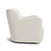 Beige upholstered chair with cylindrical bolster pillow at an upholstered bed in a light, serene bedroom setting.